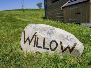 Une pierre sur laquelle est peint le mot « WILLOW », posée sur de l’herbe, avec une structure en bois en arrière-plan.