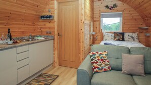 Interior acogedor de una cabaña con detalles de madera, una kitchenette, un sofá y una ventana con vistas a la vegetación.