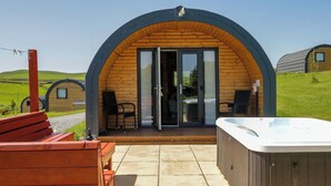 Una estructura arqueada de madera con puerta de cristal, un jacuzzi y una terraza de madera con sillas.