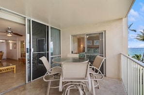 A balcony with a glass door leading to a room, a round table with chairs, and a view of the ocean. - Royal Mauian, #317 2 Bedroom Condo by RedAwning (Kihei)