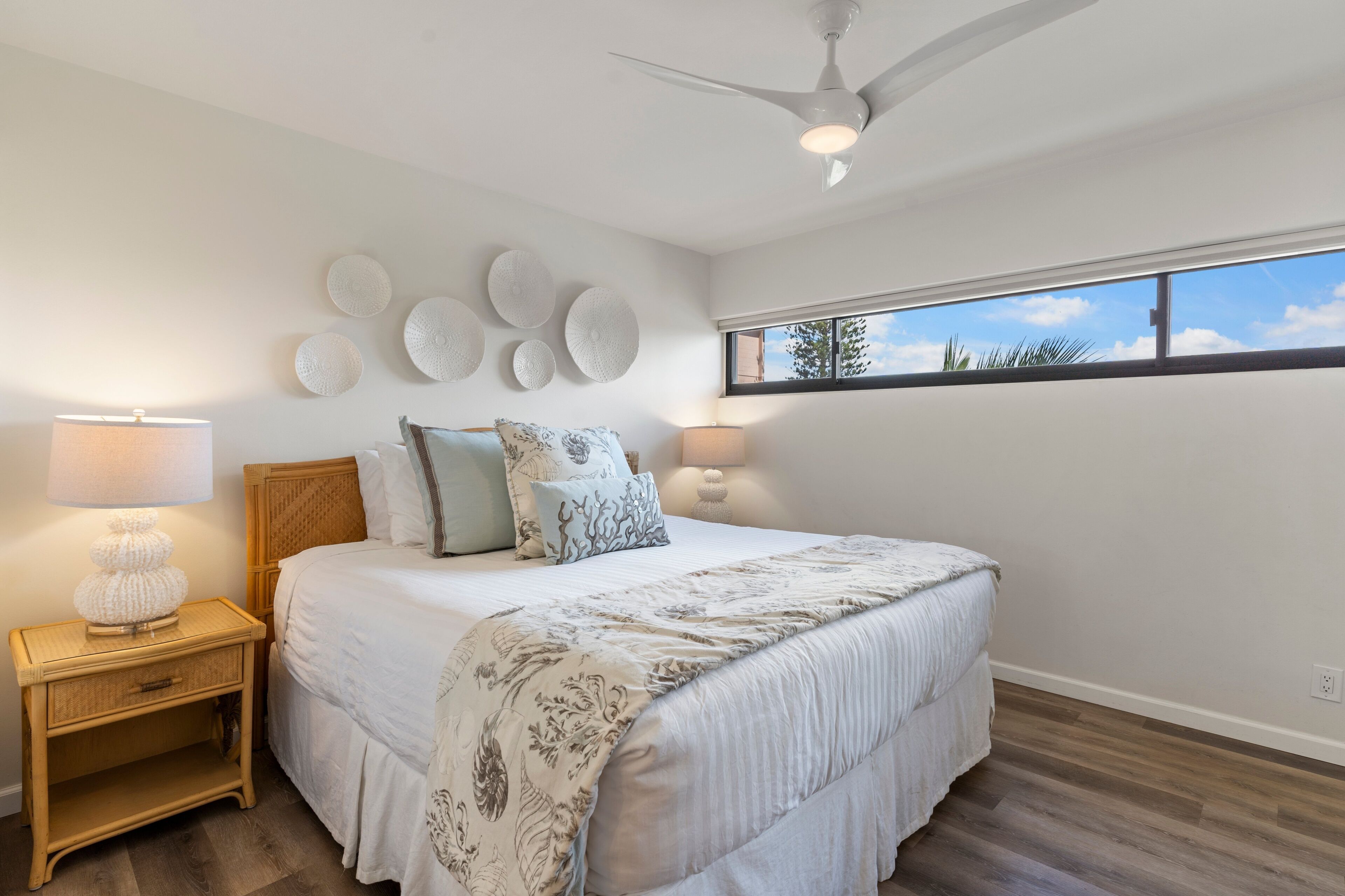 Un dormitorio con cama, mesitas de noche, decoración en la pared y ventana con vistas.