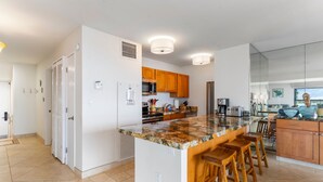 A modern kitchen with a central island, wooden bar stools, and a view of the outdoors. - Sugar Beach Resort, #535^ 2 Bedroom Condo by RedAwning (Kihei)