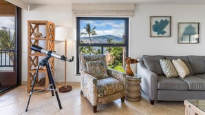 A living room with a telescope, a sofa, a chair, and a window with a view of mountains. - Sugar Beach Resort, #535^ 2 Bedroom Condo by RedAwning (Kihei)