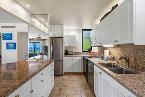 A modern kitchen with white cabinets, granite countertops, stainless steel appliances, and a view of the ocean.