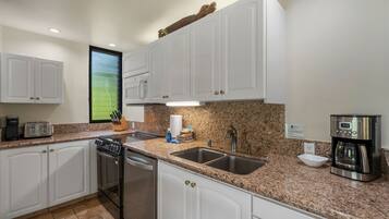 A modern kitchen with white cabinets, granite countertops, stainless steel appliances, and a built-in dishwasher.