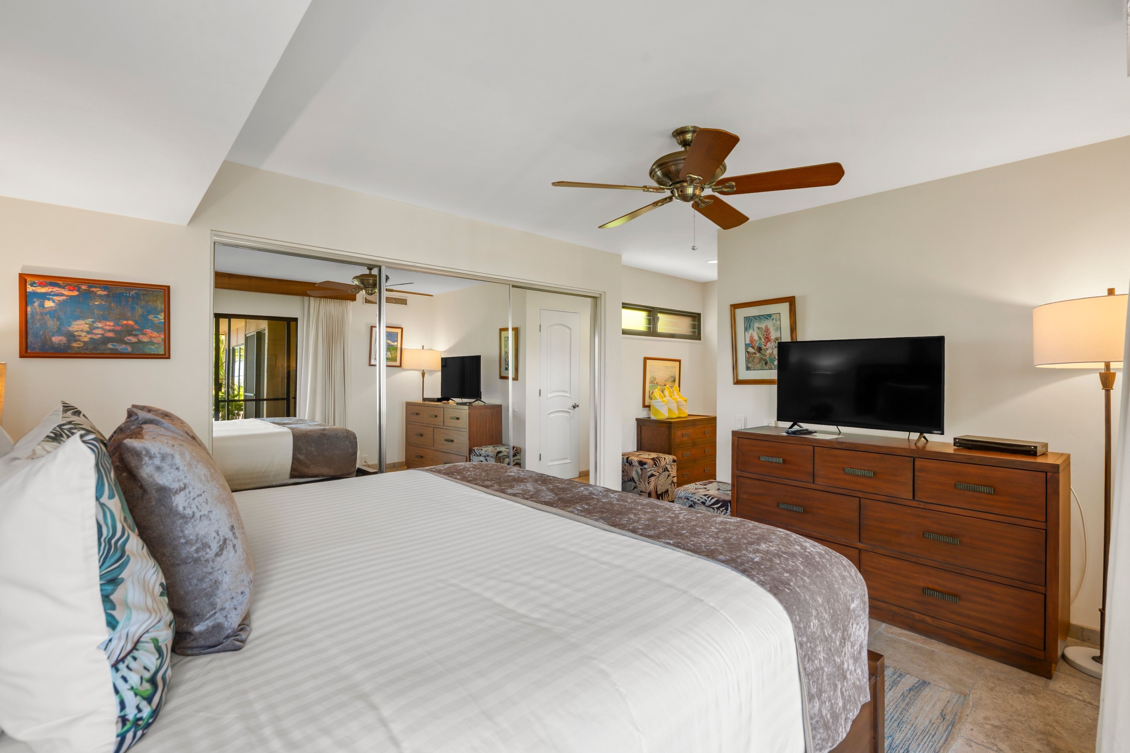 A bedroom with a large bed, a ceiling fan, a TV, and a dresser.
