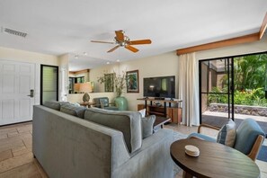A modern living room with a sofa, TV, ceiling fan, and a view of greenery outside. - Wailea Elua, #1601 1 Bedroom Condo by RedAwning (Kihei)