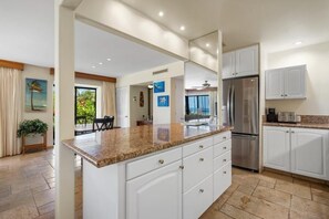 Una cocina moderna con gabinetes blancos, encimeras de granito y electrodomésticos de acero inoxidable.