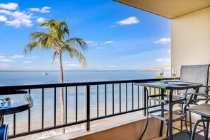 A balcony with a view of the sea, a palm tree, and a table with chairs. - Sugar Beach Resort, #ph27 1 Bedroom Condo by RedAwning (Kihei)