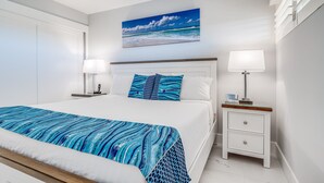 A bedroom with a bed, bedside tables, a nightstand, a painting of a beach scene, and a ceiling fan. - Sugar Beach Resort, #ph27 1 Bedroom Condo by RedAwning (Kihei)