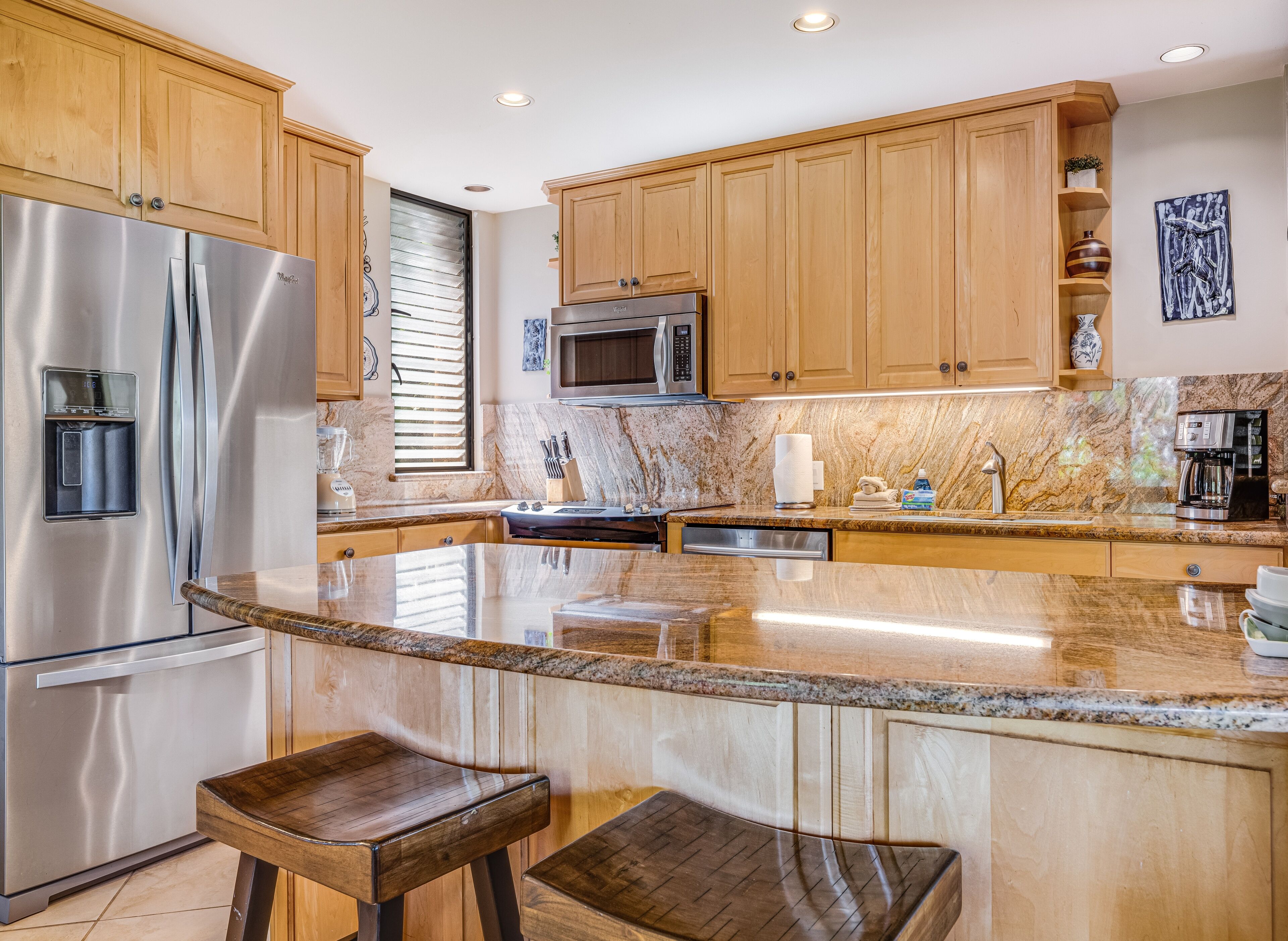 A modern kitchen with stainless steel appliances, wooden cabinets, a granite countertop, and a bar stool.