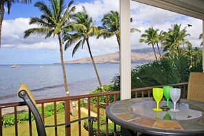 A balcony with a view of the ocean and palm trees, a round table with three glasses, and a chair. - Kihei Beach, #303 1 Bedroom Condo by RedAwning (Kihei)
