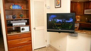 Una habitación con un televisor montado en la pared, un aparador de madera con objetos diversos y una puerta.