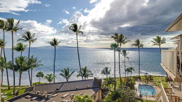 Un resort con piscina, sillas de descanso y palmeras con vista al océano.