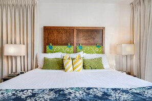 A hotel room with a large bed, green and white patterned pillows, a wooden headboard, and two bedside lamps. - Kamaole Nalu, #601 2 Bedroom Condo by RedAwning (Kihei)