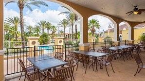 Eine Außenpatio mit Tischen und Stühlen, im Hintergrund ein Pool und Palmen.