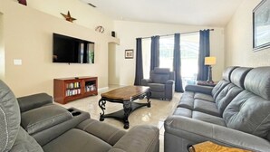 A living room with a sofa set, a coffee table, a TV mounted on the wall, and a bookshelf.