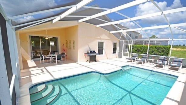 A swimming pool with a sunshade structure, outdoor seating, and a view of the surrounding landscape.