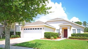 A two-story house with a garage, a red door, and a well-maintained lawn.