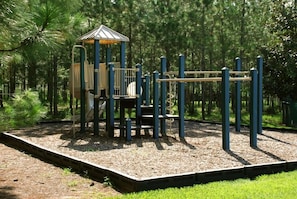 Explore the playground's climbing tower, slide, and balancing equipment set amidst a lush wooded area.