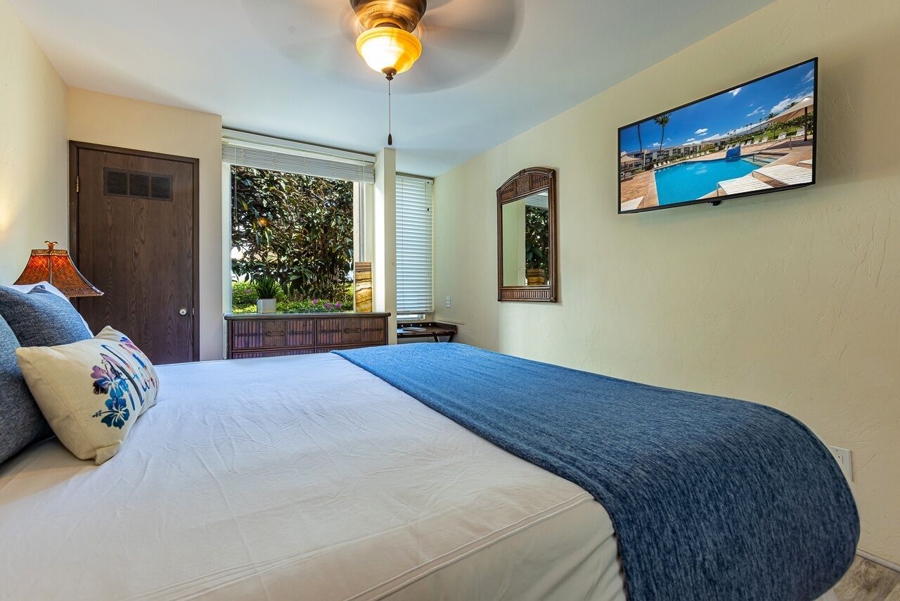 A bedroom with a bed, a ceiling fan, a TV, a window with blinds, and a view of a pool outside.