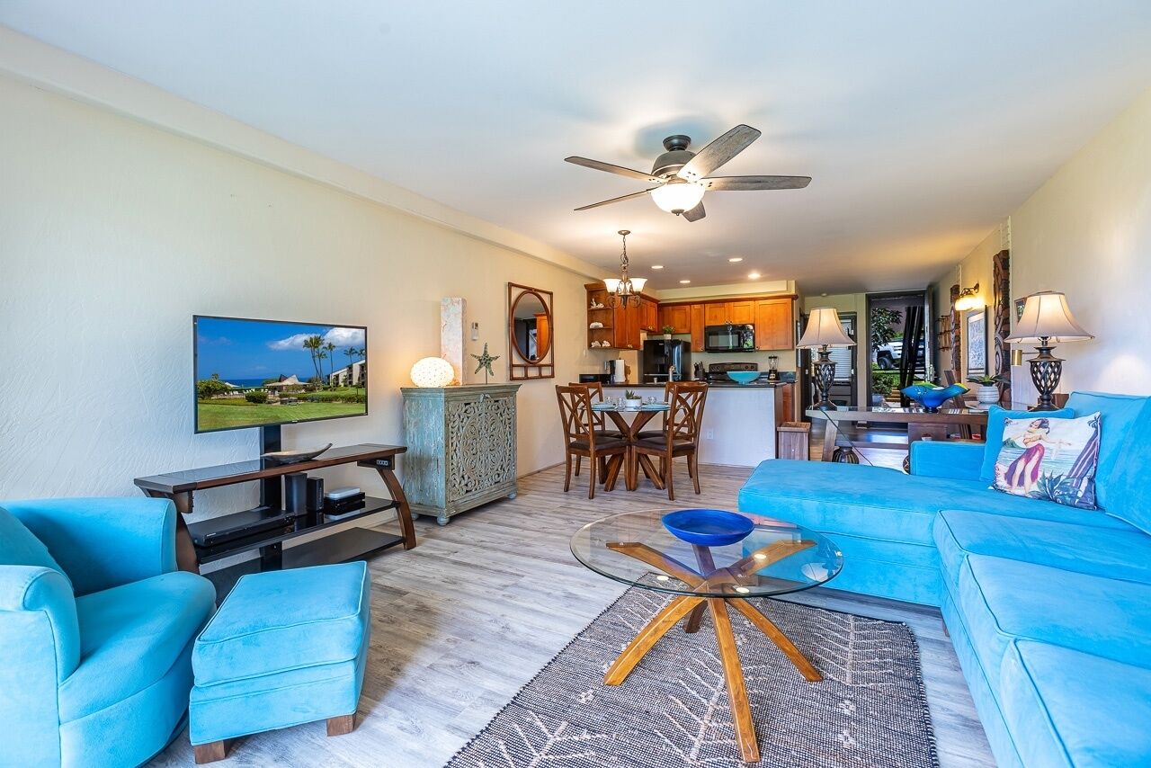 A modern living room with a blue sofa, a glass coffee table, and a television.
