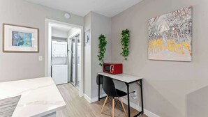Une pièce moderne avec une table blanche, un micro-ondes rouge, une chaise noire et un tableau accroché au mur.