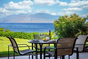 An outdoor dining area with a table set for two, overlooking a body of water and a mountain range. - Makena Surf, #f-110 2 Bedroom Condo by RedAwning (Kihei)