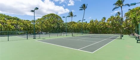 Un court de tennis doté d’une surface verte, entouré d’arbres et surplombé d’un ciel dégagé.
