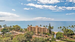 A coastal hotel with multiple floors, a parking area, and a view of the sea and distant mountains. - Kihei Beach, #307 1 Bedroom Condo by RedAwning (Kihei)