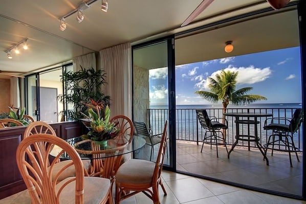 A balcony with a table and chairs, a potted plant, and a view of the sea.