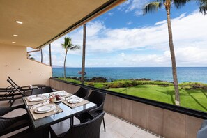 A dining area with a table set for four, overlooking a coastal view with palm trees and the ocean. - Makena Surf, #f-209 2 Bedroom Condo by RedAwning (Kihei)