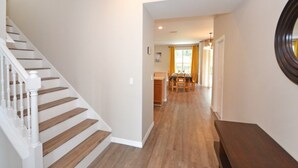 Un pasillo con una escalera de madera, una zona de comedor y una cocina al fondo.