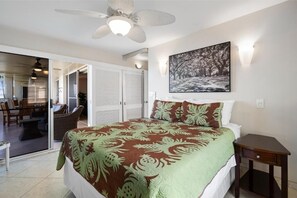 Ein Schlafzimmer mit einem Bett, einem Deckenventilator, einem Gemälde und einer Schiebetür, die auf einen Balkon führt.