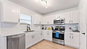 A modern kitchen with white cabinets, stainless steel appliances, and a herringbone tile backsplash.
