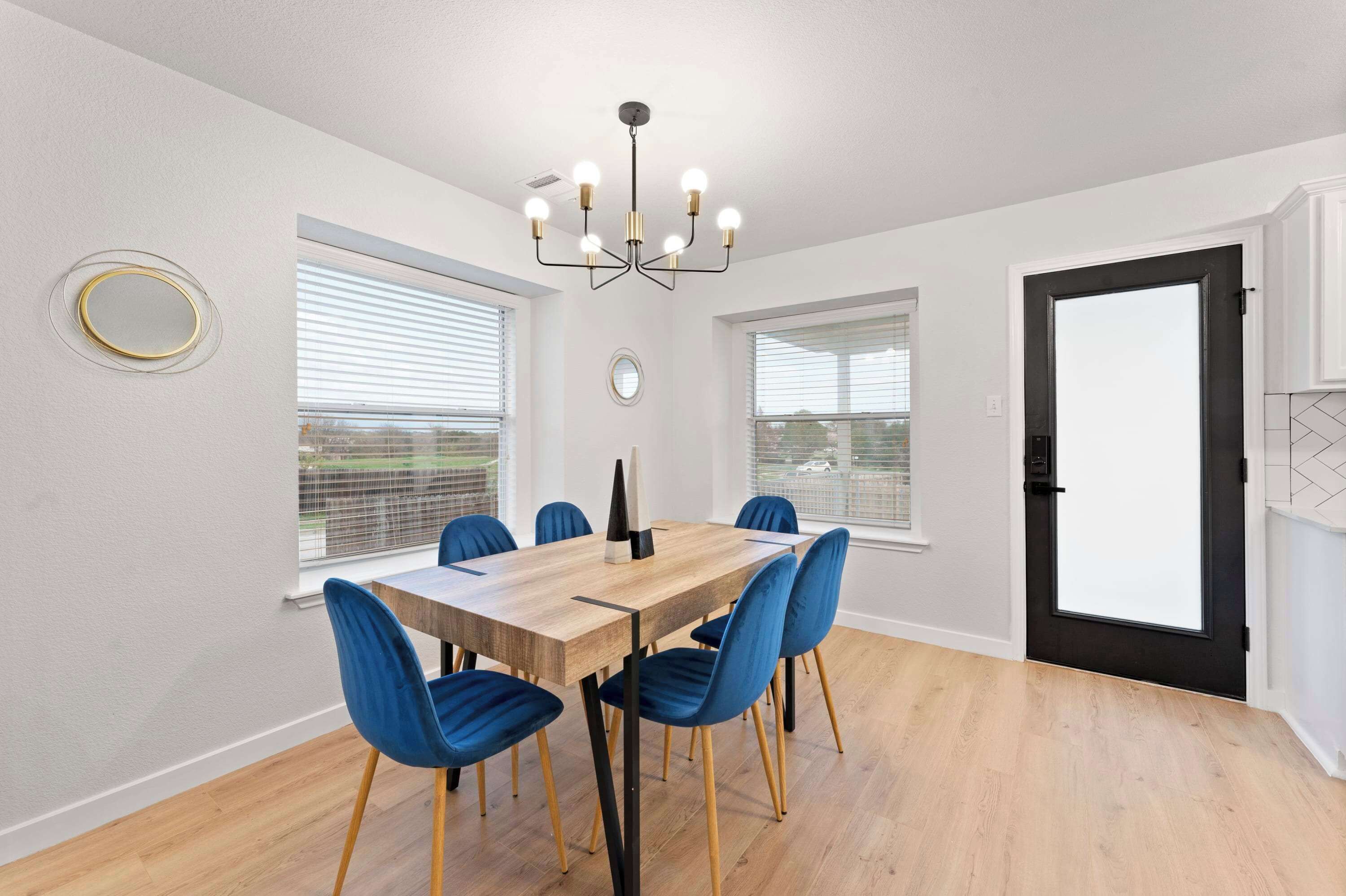 A dining room with a wooden table, blue chairs, a chandelier, and large windows.