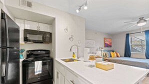 Una cocina moderna con refrigerador, estufa, microondas y pileta. Hay un comedor con mesa y sillas, y una cama con vista al exterior.