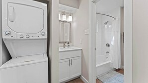 Un área de lavandería con lavadora y secadora, un baño con lavamanos, espejo y ducha.