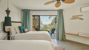 A bedroom with two beds, a ceiling fan, a view of palm trees and the sea, and a balcony with a chair. - Catalina Tropical Lodge (Cabrera)