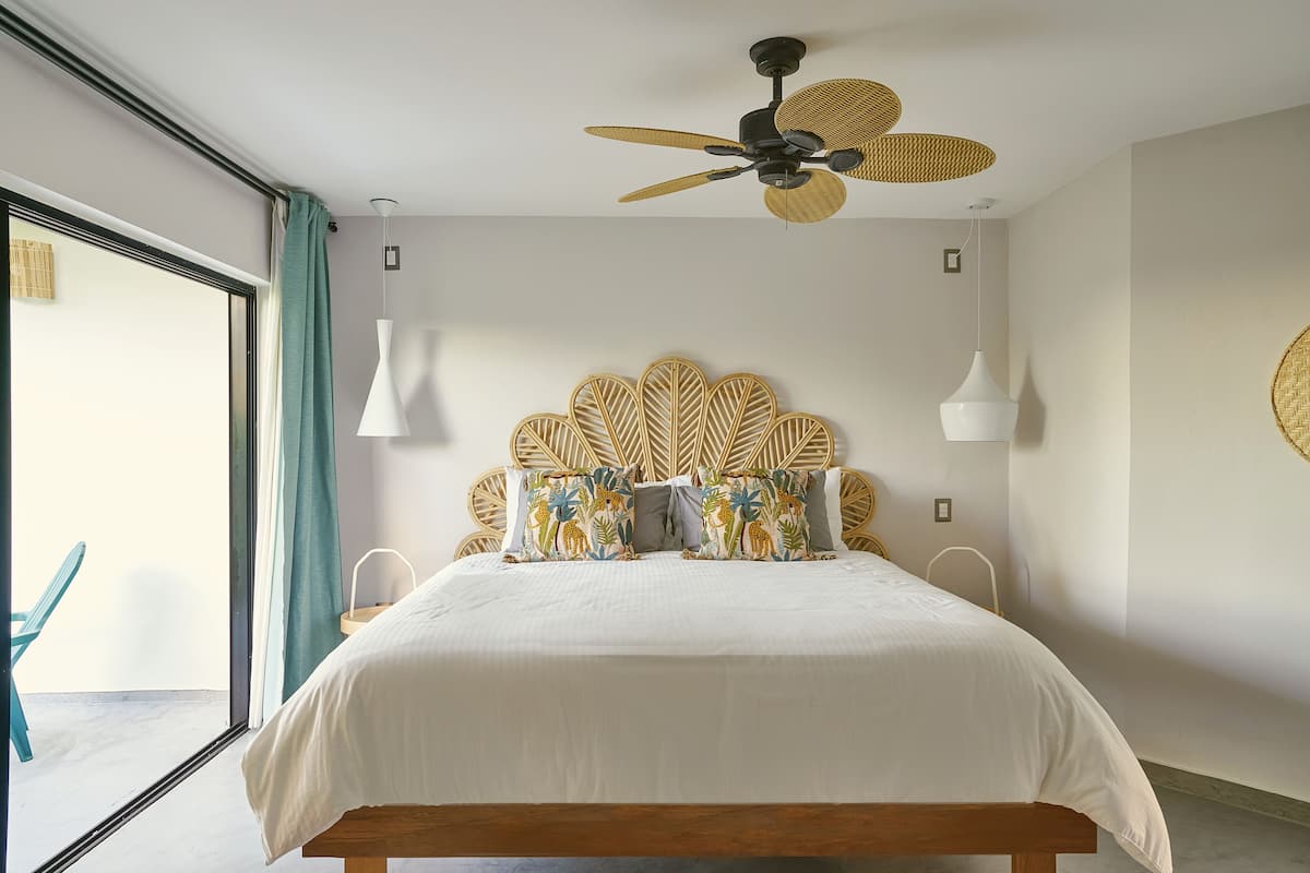 A bedroom with a bed, a ceiling fan, a wall-mounted light, and a view through a window.