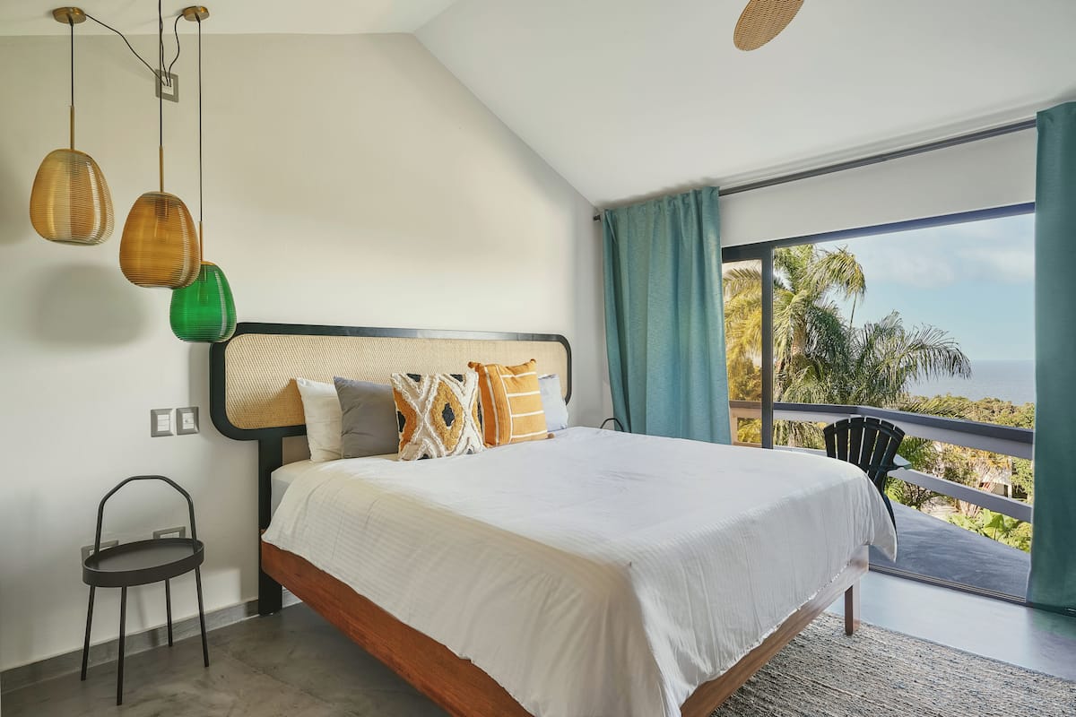 A bedroom with a large bed, a chair, and a balcony with a view.