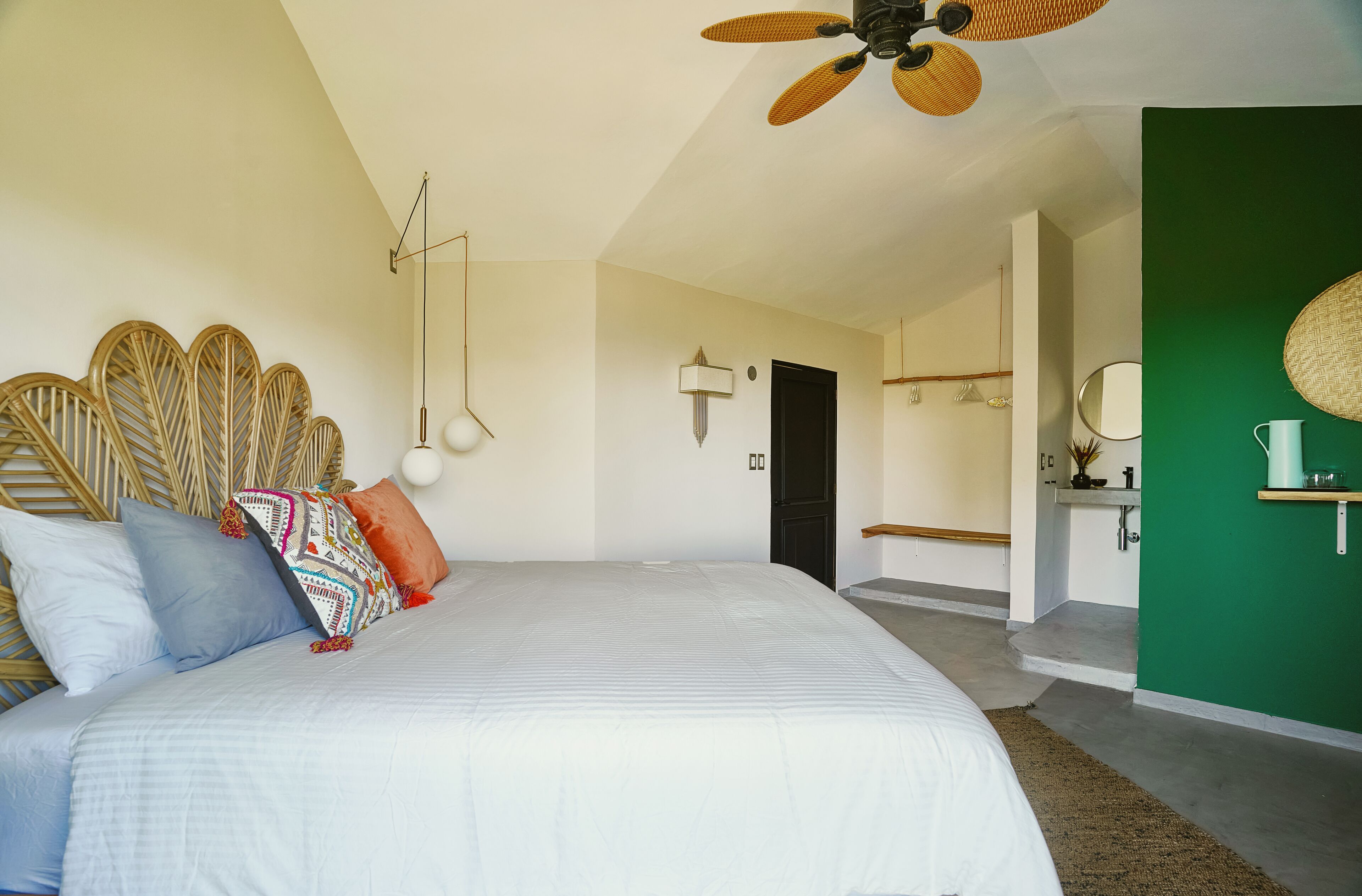 Ein Schlafzimmer mit einem Bett, Kissen, einem Deckenventilator, einer Wandlampe und einer grünen Akzentwand.