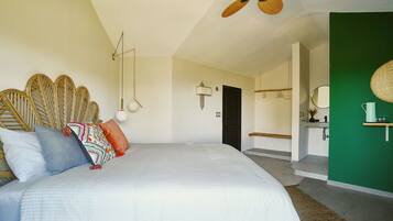 Une chambre à coucher avec un lit, des oreillers, un ventilateur de plafond, une lampe fixée au mur et un mur d’accent de couleur verte.