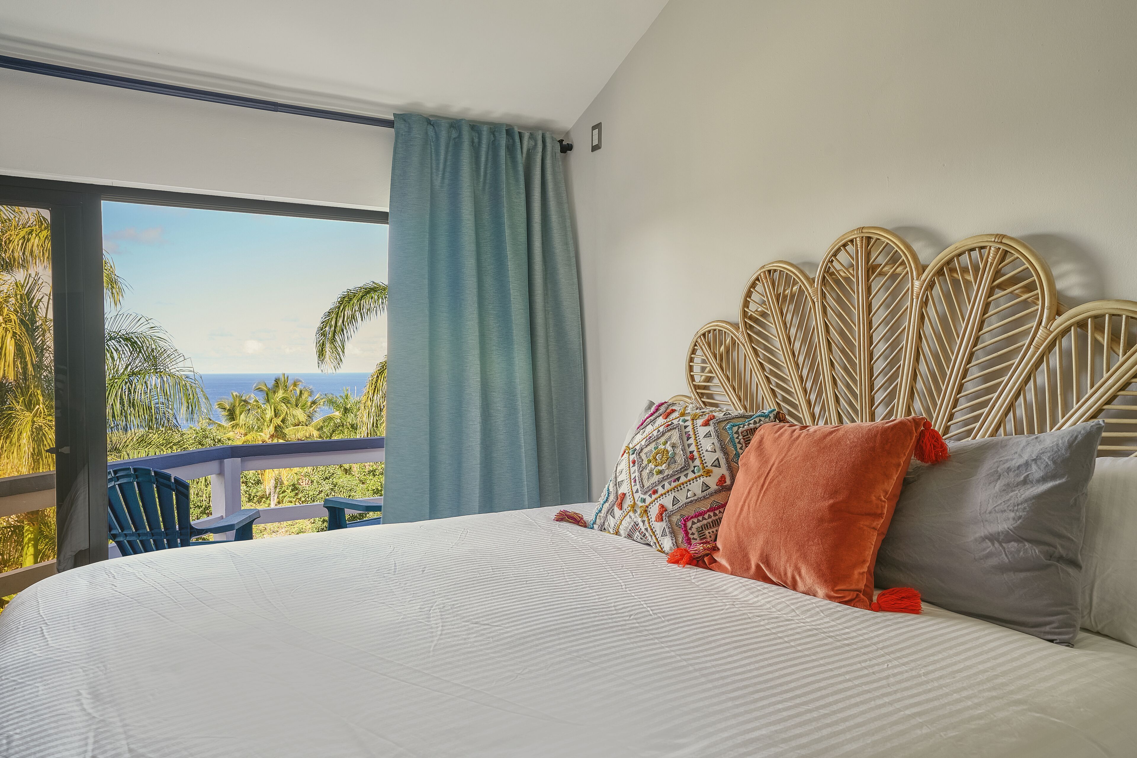 Un dormitorio con una cama grande, un cabecero de mimbre y vistas a palmeras y al océano.