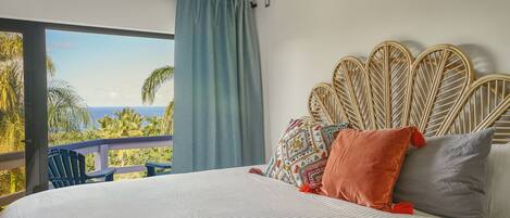 Un dormitorio con una cama grande, un cabecero de mimbre y vistas a palmeras y al océano.