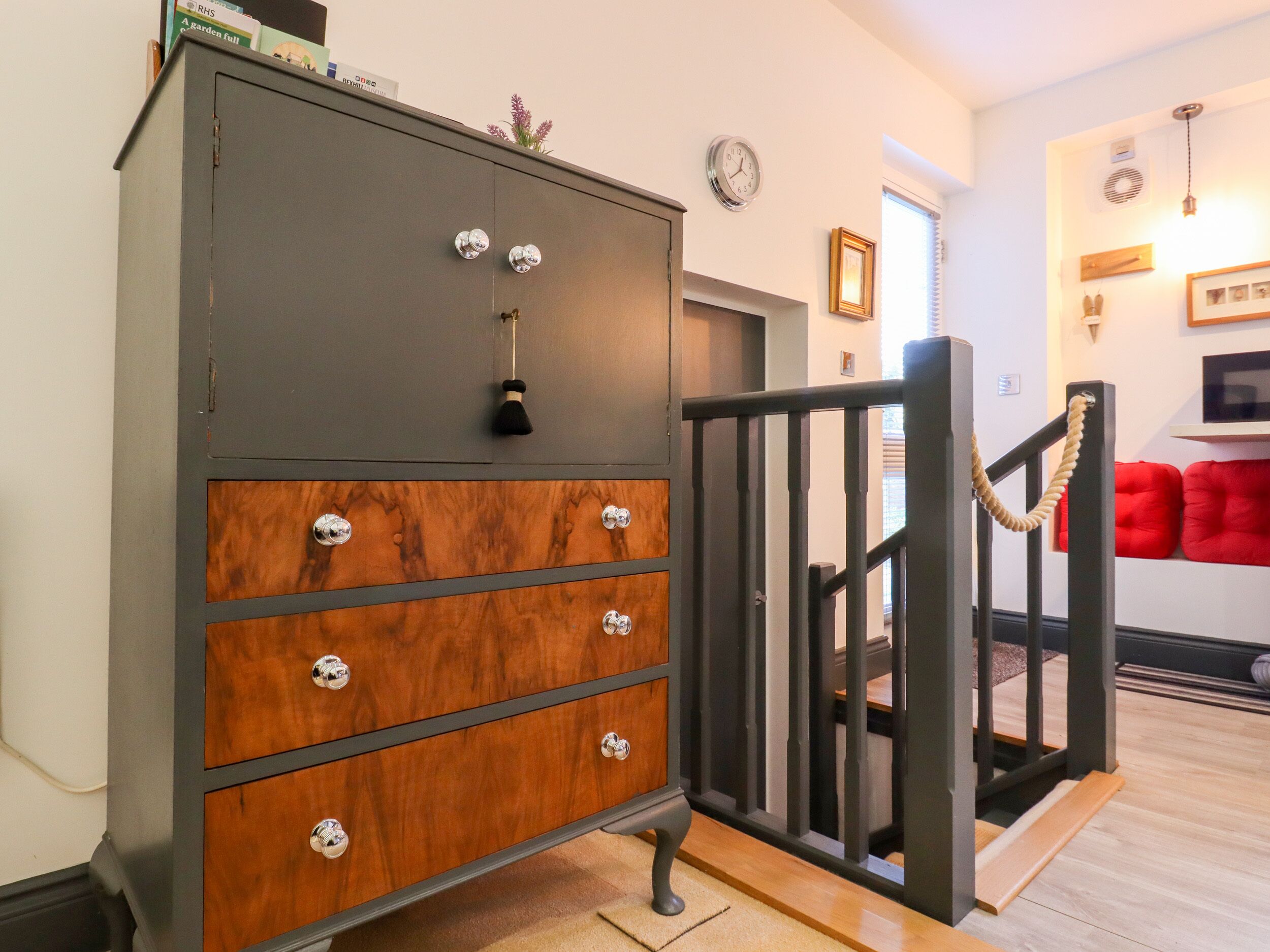 Een grijze, houten dressoir met meerdere lades en een zwart leuning in een kamer met een houten vloer, met een rode bank op de achtergrond.