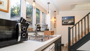 Una cocina moderna con microondas integrado, lavavajillas y un fregadero. Hay lámparas colgantes y una ventana que proporciona luz natural.