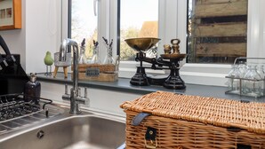 Una cocina con un lavamanos de acero inoxidable, una estufa, una ventana con vistas a un edificio y varios utensilios de cocina en el alféizar.
