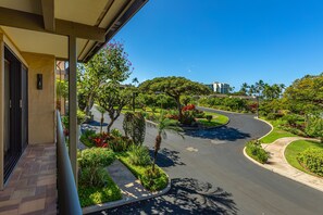 Une route sinueuse bordée de jardins aménagés, avec un bâtiment visible au loin.