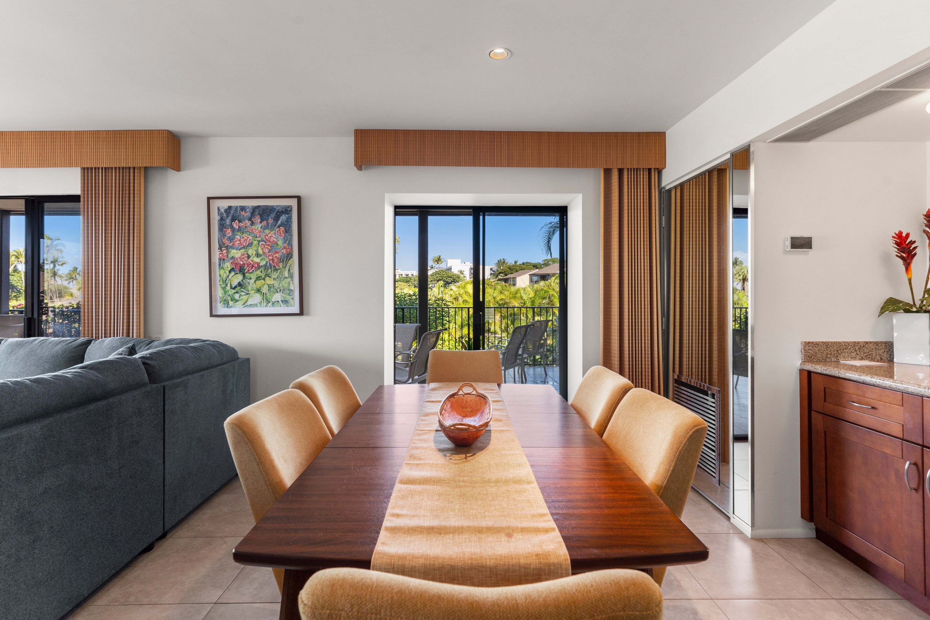 Un comedor moderno con una mesa de madera, sillas color beige y vistas a zonas verdes a través de grandes ventanales.